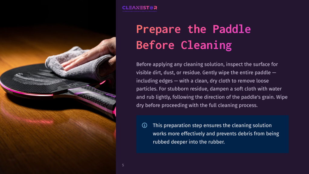 A Hand Gently Wipes A Ping Pong Paddle With A Soft Cloth, Preparing It For Cleaning. The Paddle Has A Black Surface With Subtle Purple Accents And Glowing Pink Trim.