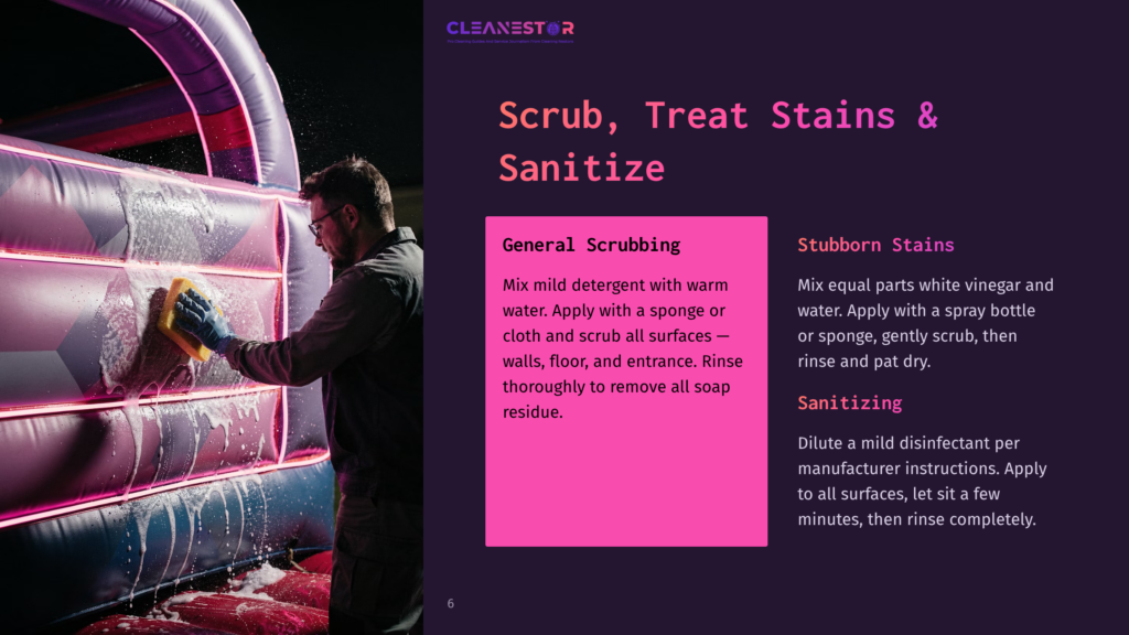 Man In Glasses And Gloves Scrubs An Inflatable Bounce House With A Yellow Sponge And Soap Suds, Cleaning Neon Pink And Purple Surfaces.