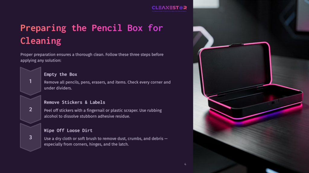 A Pink Plastic Pencil Box Is Open, Showing Pens And Erasers Inside. Nearby, A Small Brush And Cleaning Tools Are Visible On A Grey Surface.