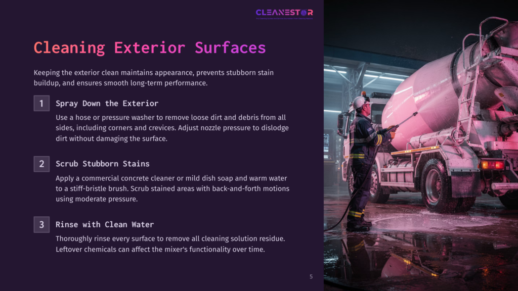 A Worker In A Yellow Hard Hat And Blue Uniform Uses A Pressure Washer To Clean A Large, Pink Cement Mixer Truck In A Dimly Lit Garage. The Truck Is Covered In White Foam And Water Sprays.