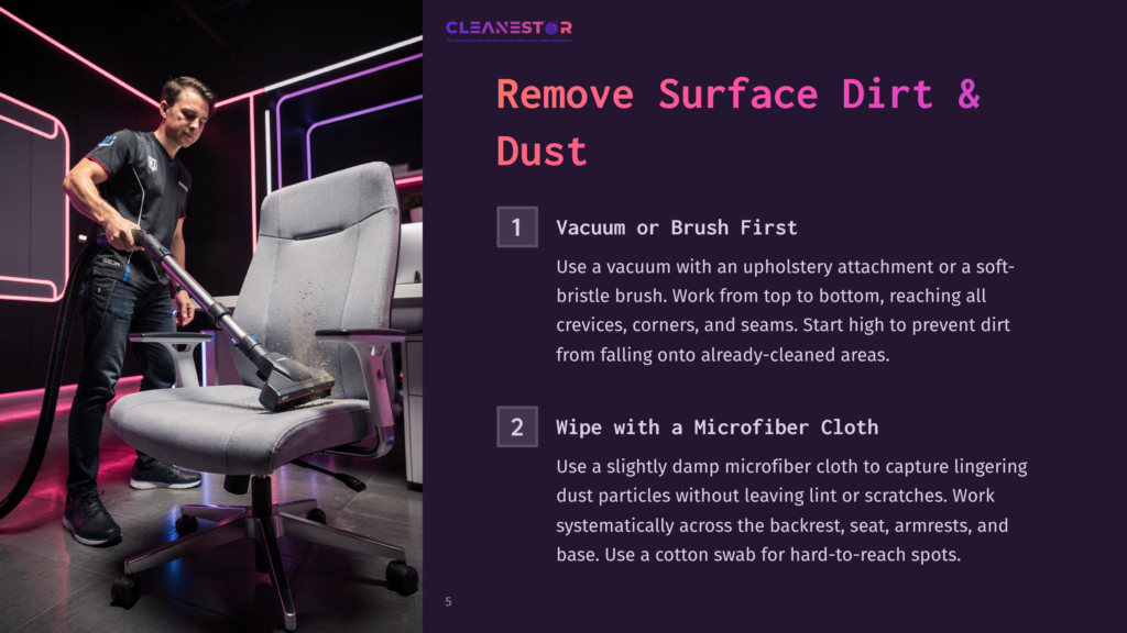 A Person Vacuuming A Gray Office Chair With An Upholstery Attachment, Demonstrating Cleaning Techniques On A Dark Background.