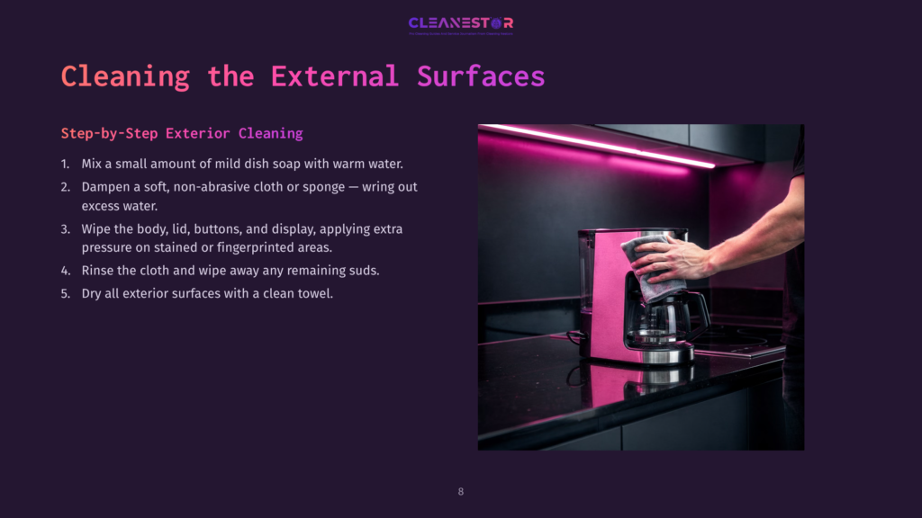 A Person'S Hands Wipe Down A Shiny Pink Coffee Maker With A Gray Cloth, Cleaning Its Exterior Surfaces. The Coffee Maker Sits On A Dark Countertop In A Modern Kitchen.